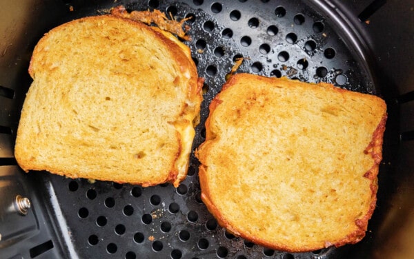 Overhead view inside an air fryer basket with two grilled cheese sandwiches.