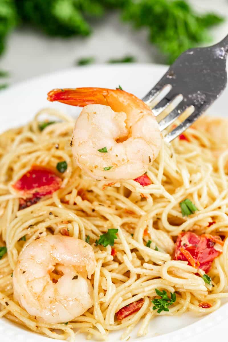 fork with a piece of shrimp hovering over a plate of pasta.