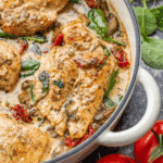A close up view of creamy tuscan chicken in a braising pan with sun-dried tomatoes and wilted spinach.