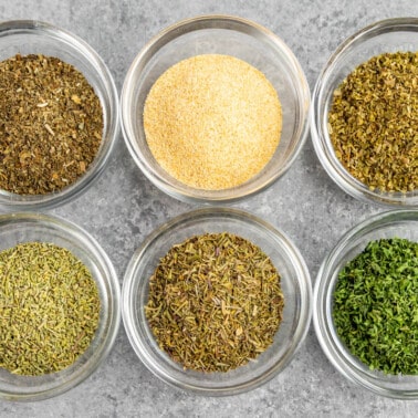 Overhead view of the individual spices used in Italian seasoning in separate glass bowls.