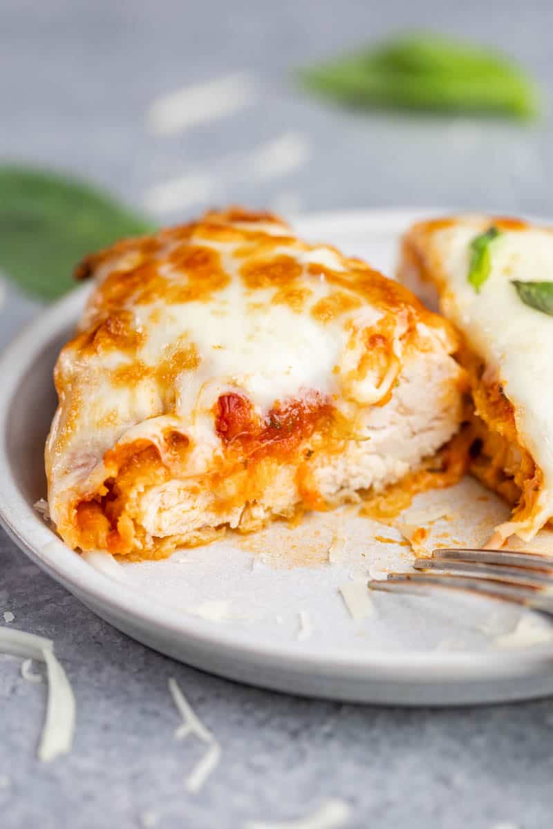 A cut in half piece of air fryer chicken parmesan on a dinner plate.