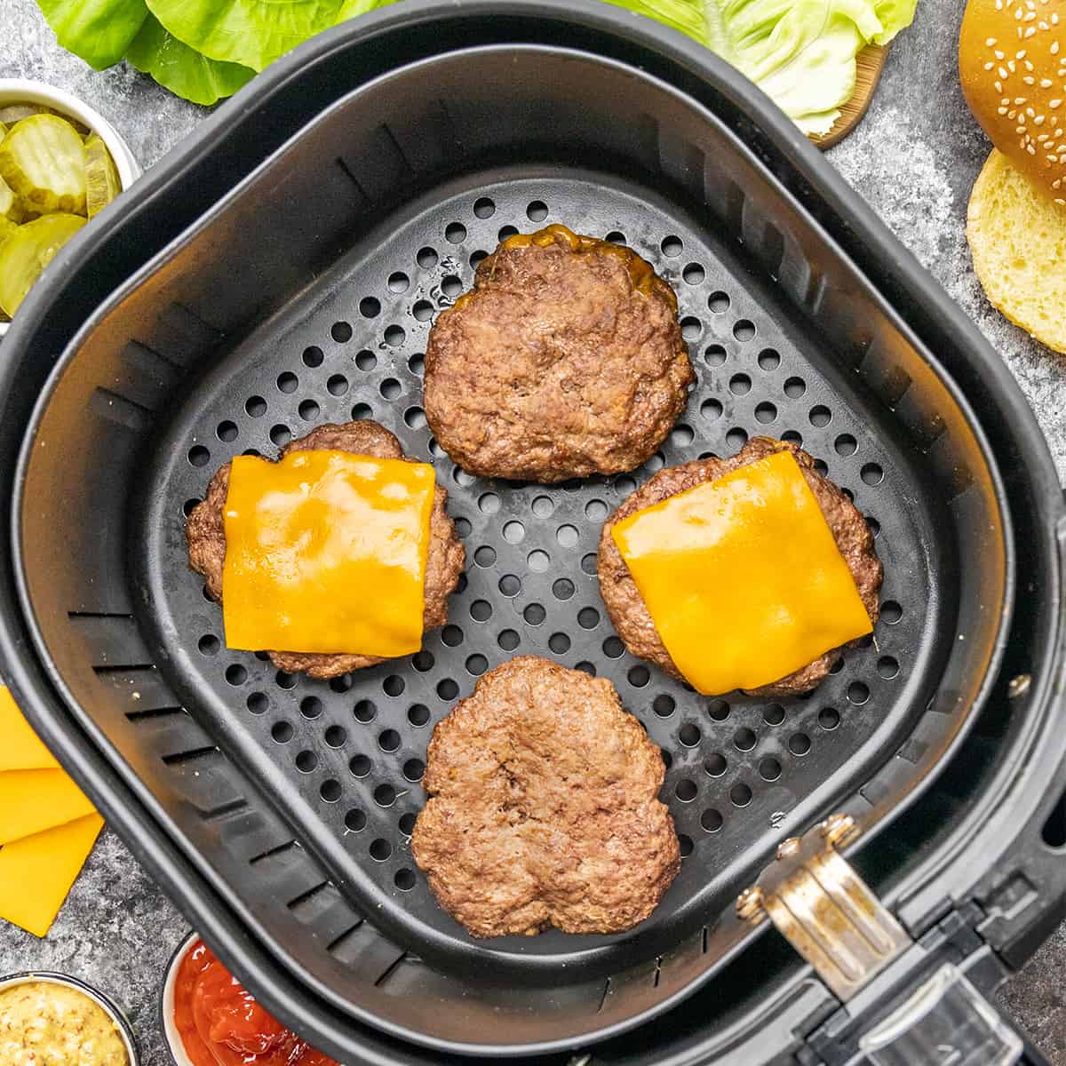Overhead view looking into an air fryer basket with hamburgers.