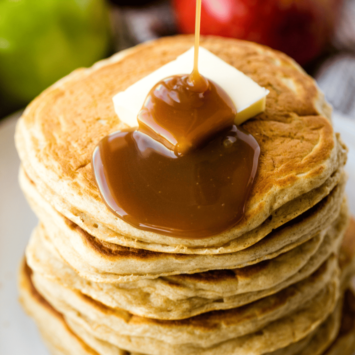 Stack of apple pancakes with caramel syrup being poured on top.