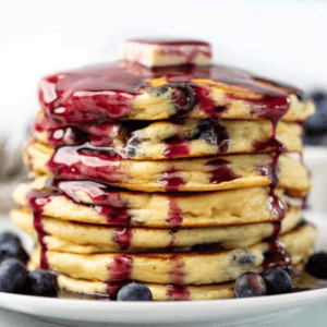 Stack of blueberry pancakes drizzled with blueberry syrup.