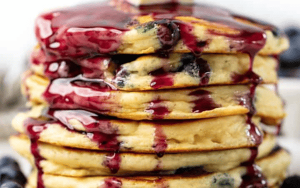 Stack of blueberry pancakes drizzled with blueberry syrup.
