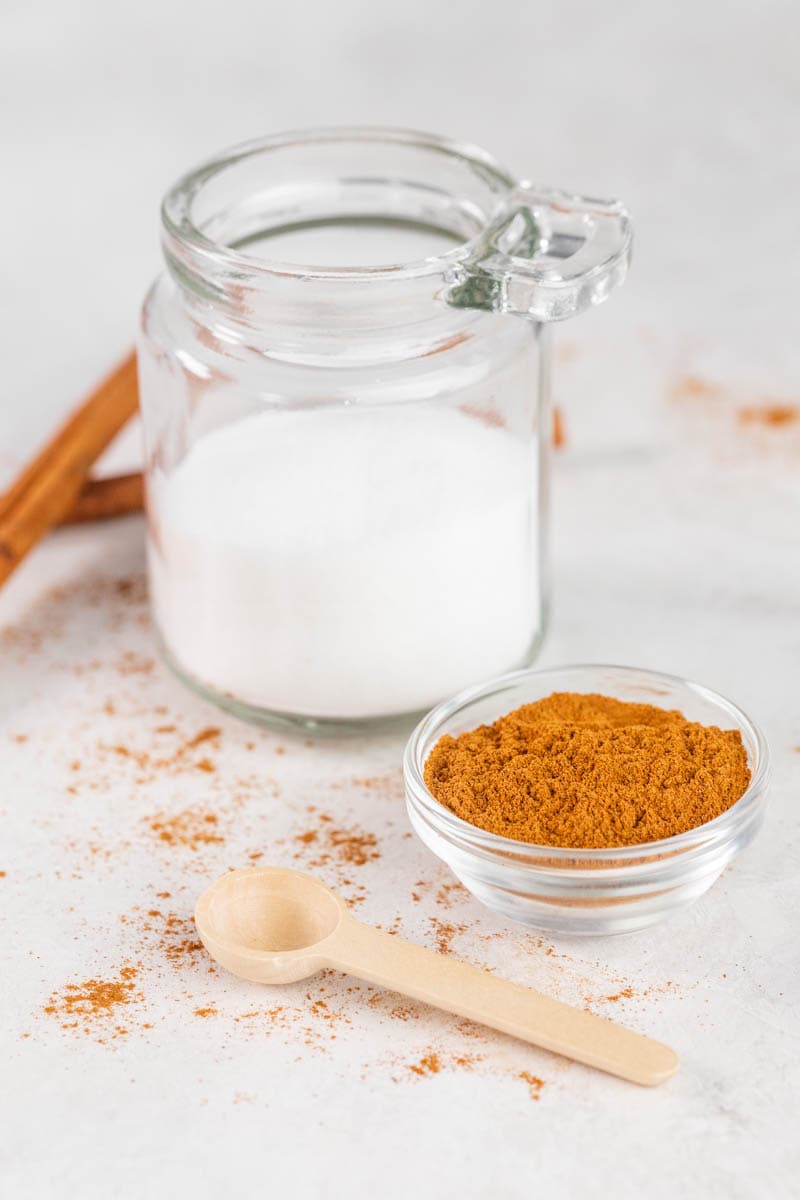 Cinnamon in a glass jar next to sugar in a jar.