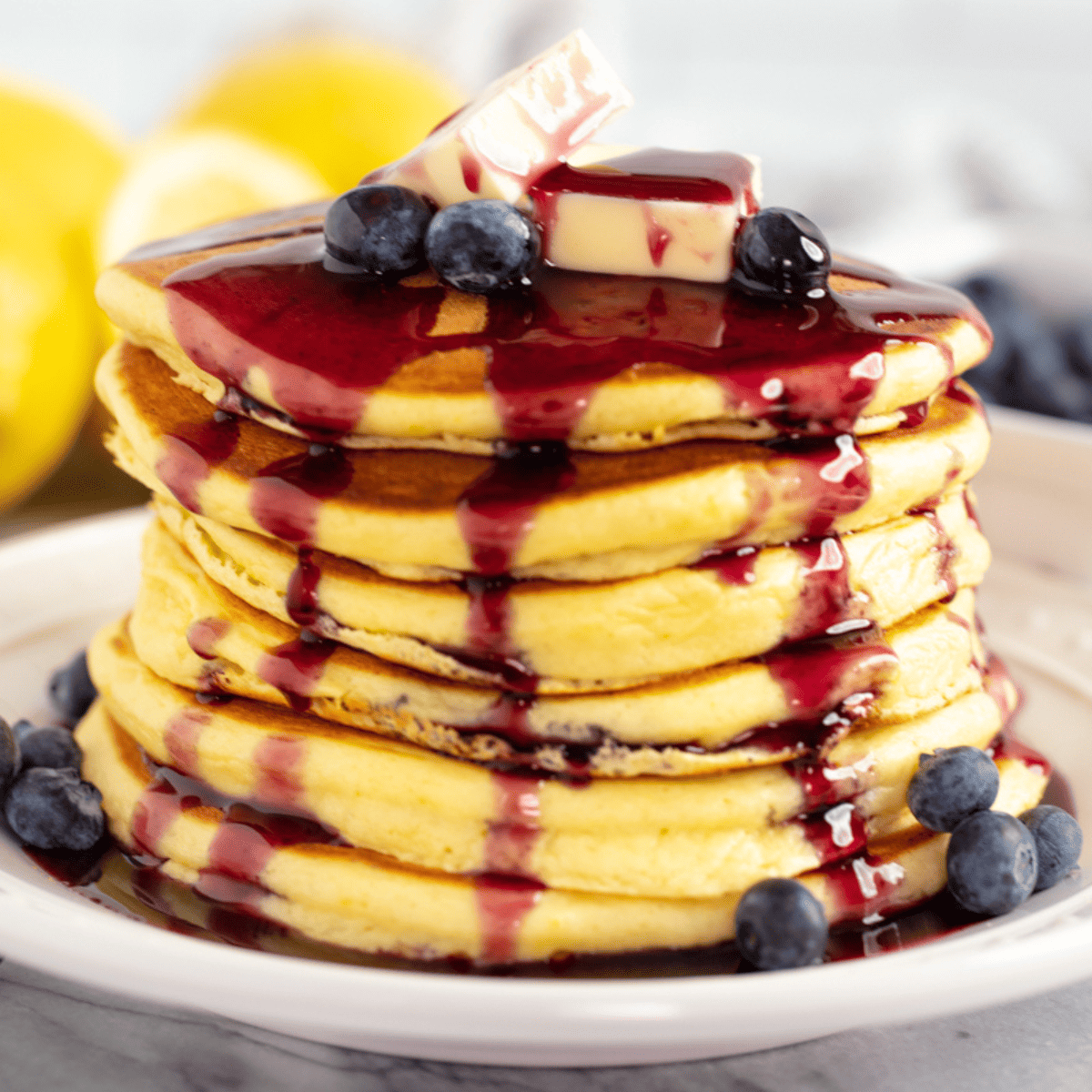 Stack of lemon ricotta pancakes topped with blueberry syrup and fresh blueberries.