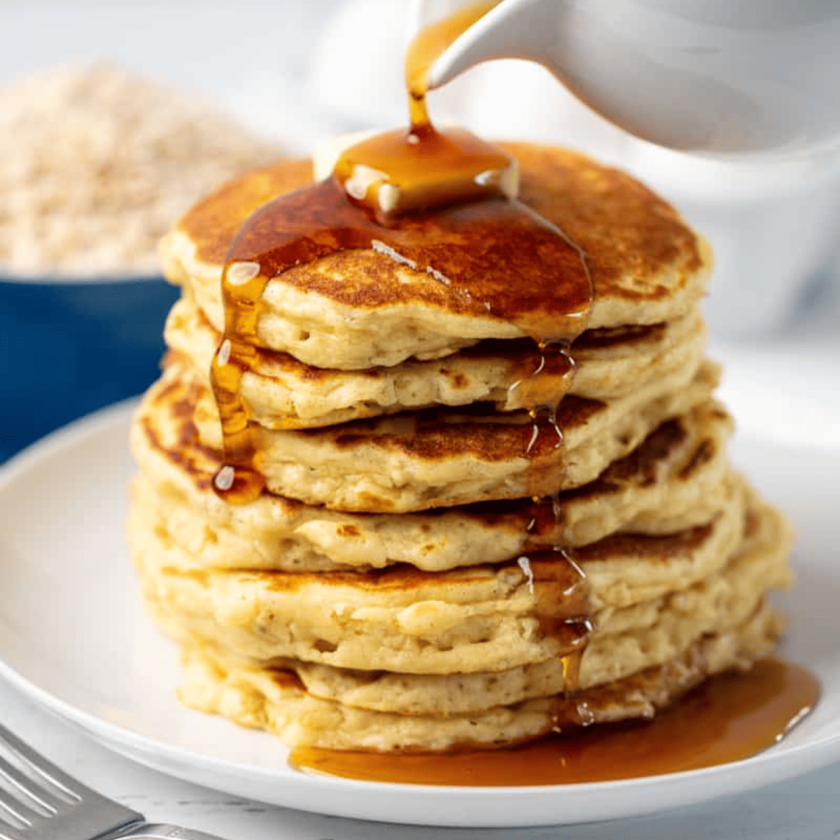 Stack of oatmeal pancakes with syrup being poured on top.