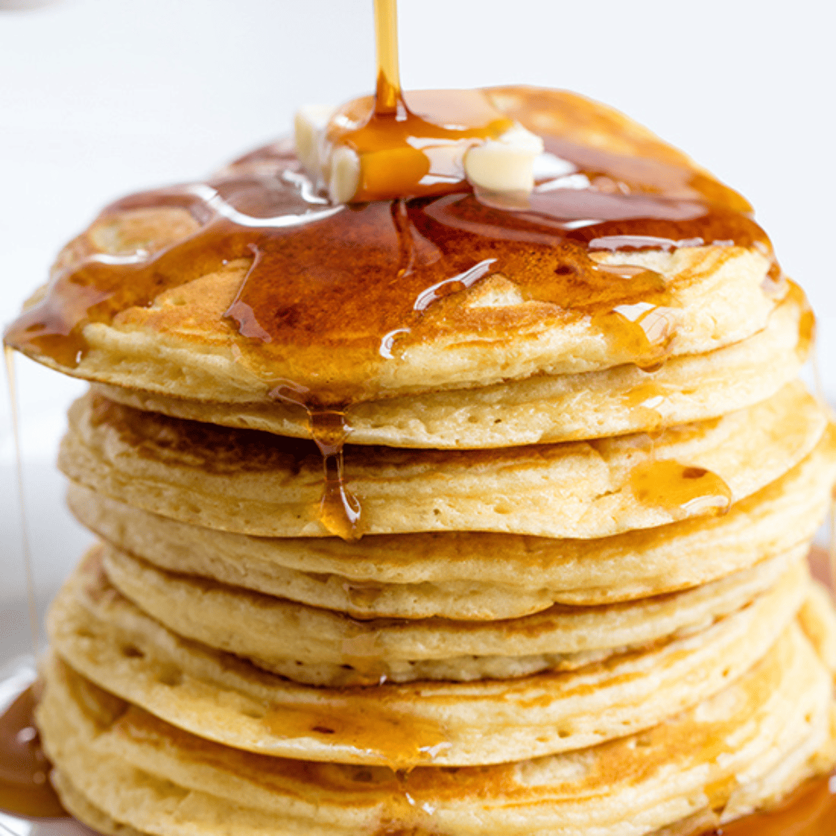A stack of pancakes with syrup being poured on top.