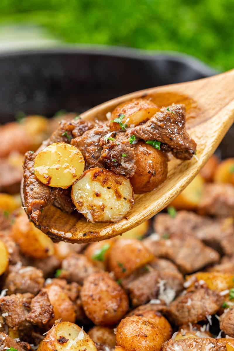 Close-up view of a wooden spoon full of steak bites and potatoes.