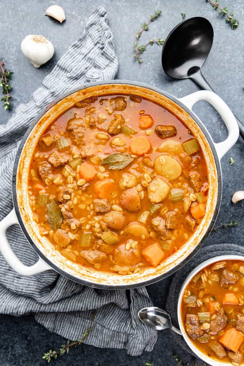 Overhead view of beef and barley soup in a large white pot.