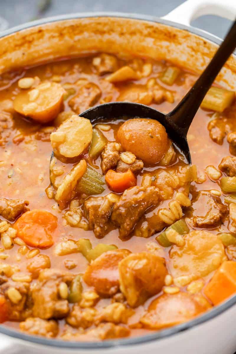 Close up view of beef and barley soup in a ladle.