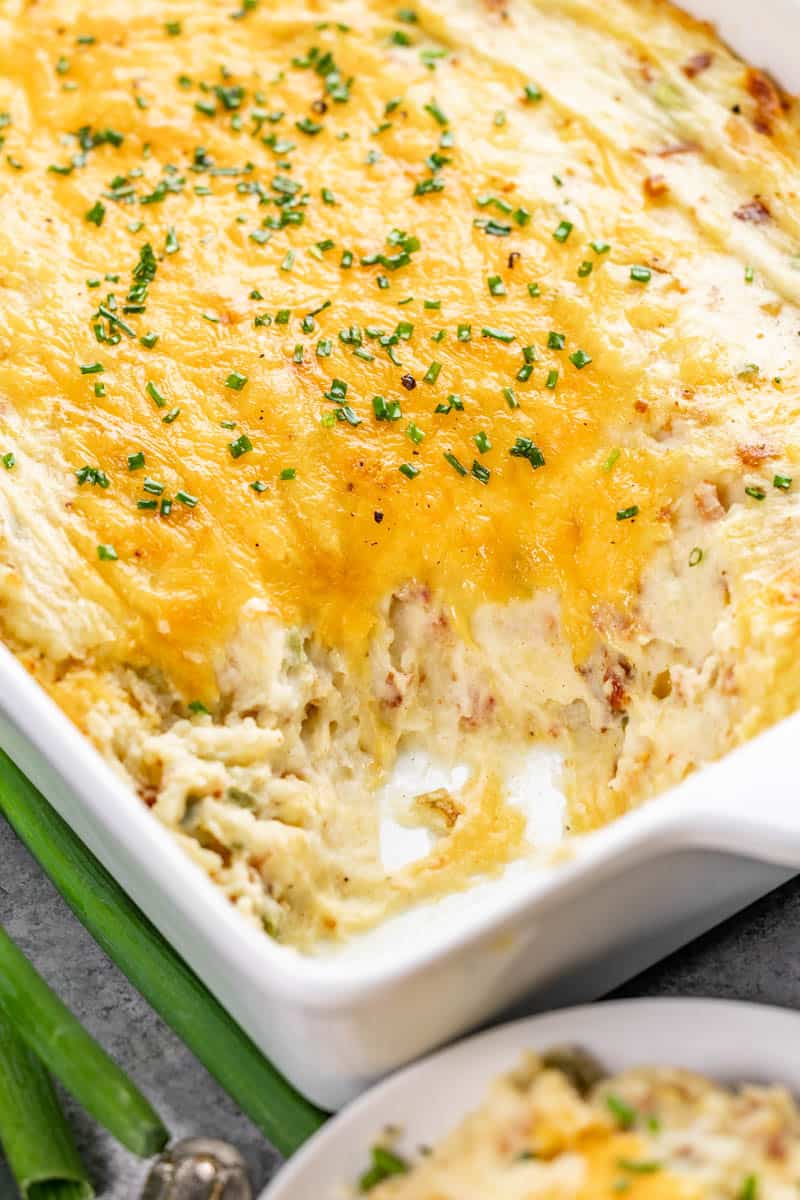 A close-up view of a twice baked potato casserole with one serving removed.