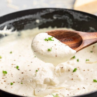 A wooden spoon filled with homemade Alfredo sauce.