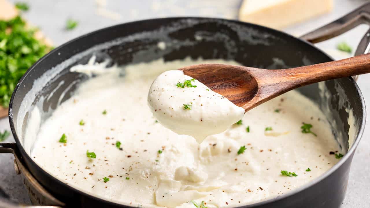 A wooden spoon filled with homemade Alfredo sauce.