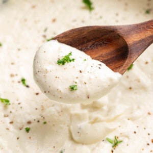 Close up view of Alfredo sauce on a wooden spoon.