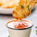 Dipping a chicken fillet with garlic and parmesan in a small cup of sauce.
