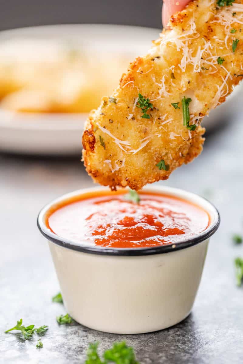 Dipping a chicken fillet with garlic and parmesan in a small cup of sauce.