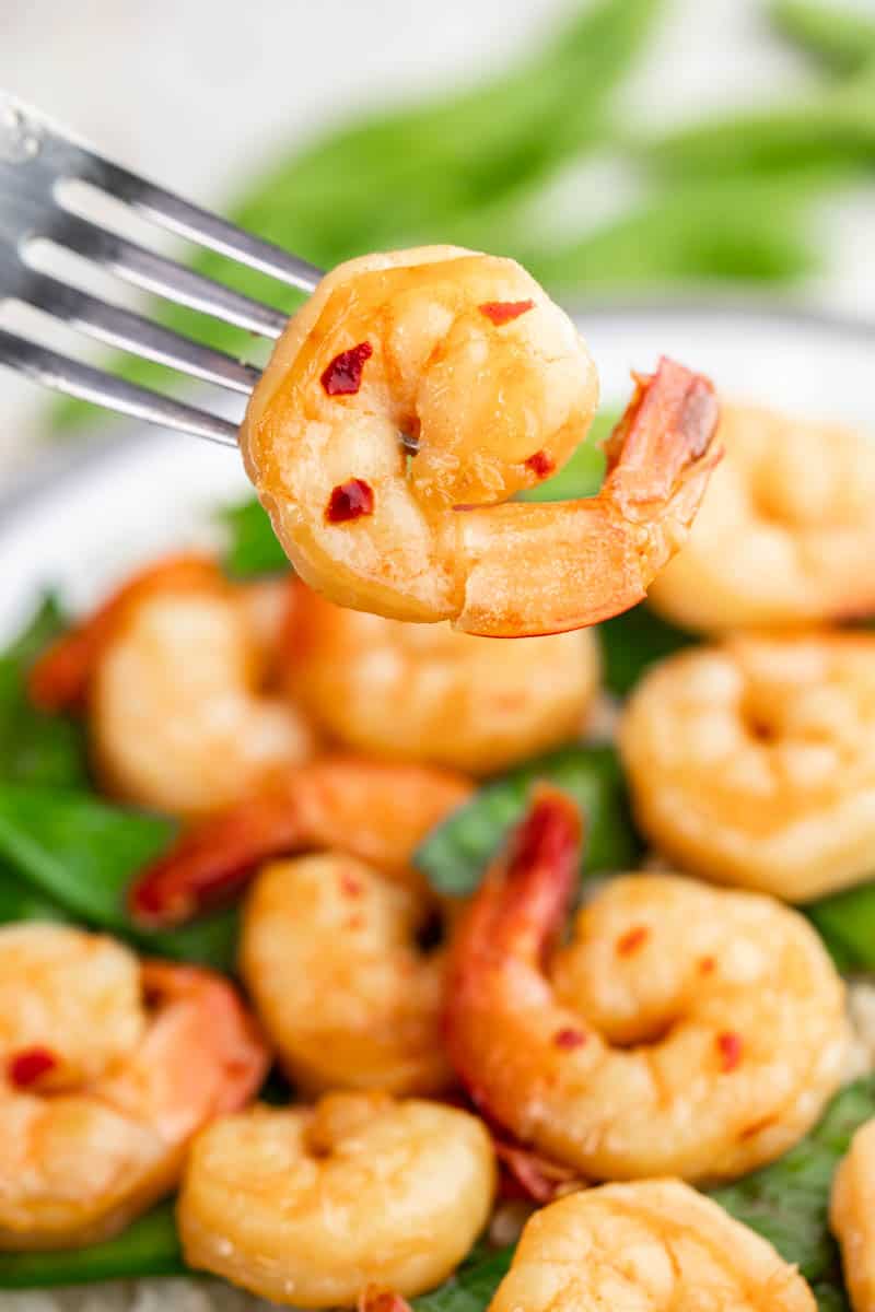 A fork holding onto a piece of honey garlic shrimp.