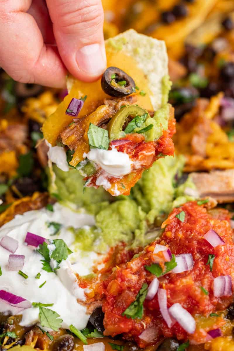 A hand holding up a chip from a pile of nachos.