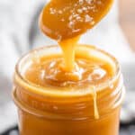 A spoon dripping sea salt caramel sauce into a glass jar.