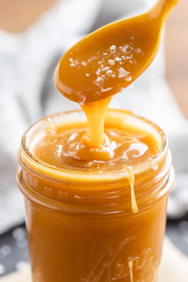 A spoon dripping sea salt caramel sauce into a glass jar.