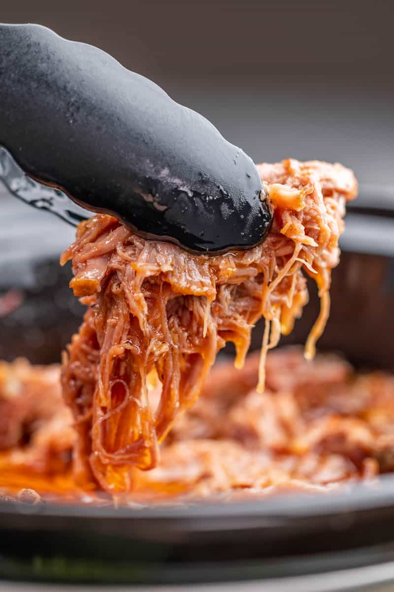 Tongs holding up a piece of sweet pulled pork.