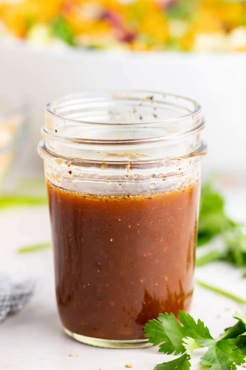 A close up view of a homemade Asian Sesame Vinaigrette in a small mason jar with a colorful salad in the background. 