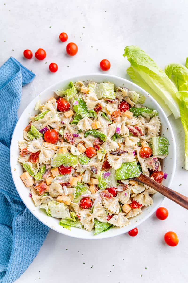 BLT pasta salad in a white bowl with a wooden spoon.