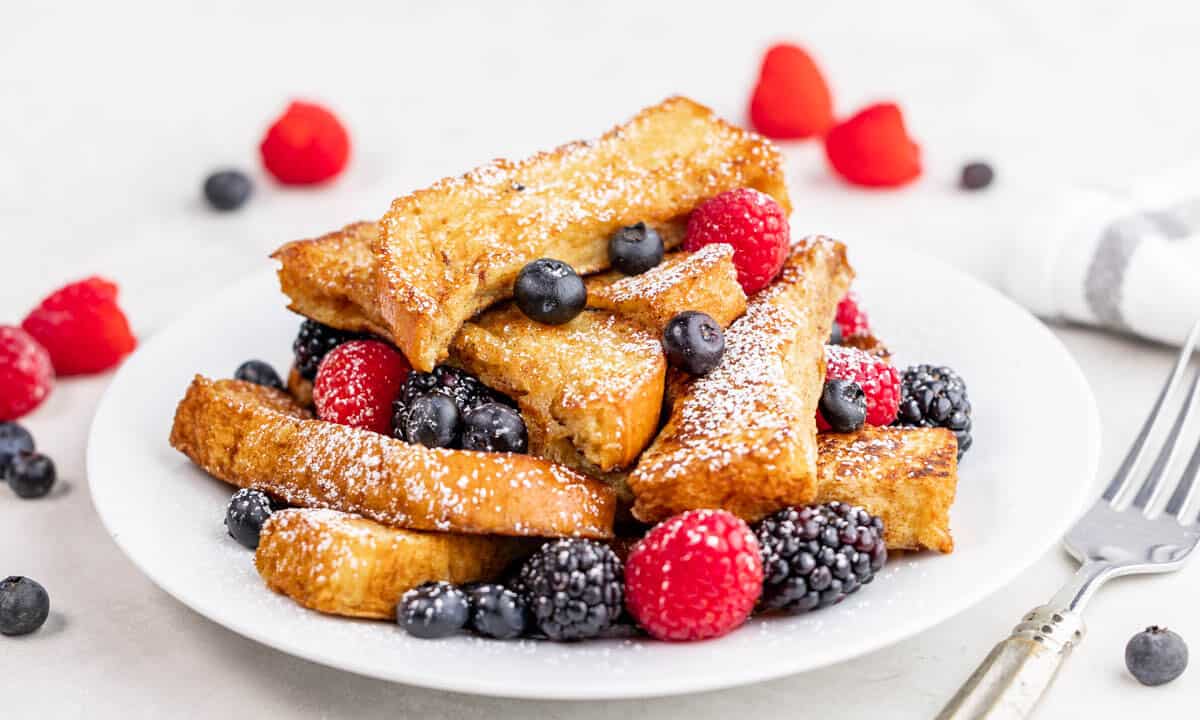 A stack of French toast sticks with fresh berries on a white plate.