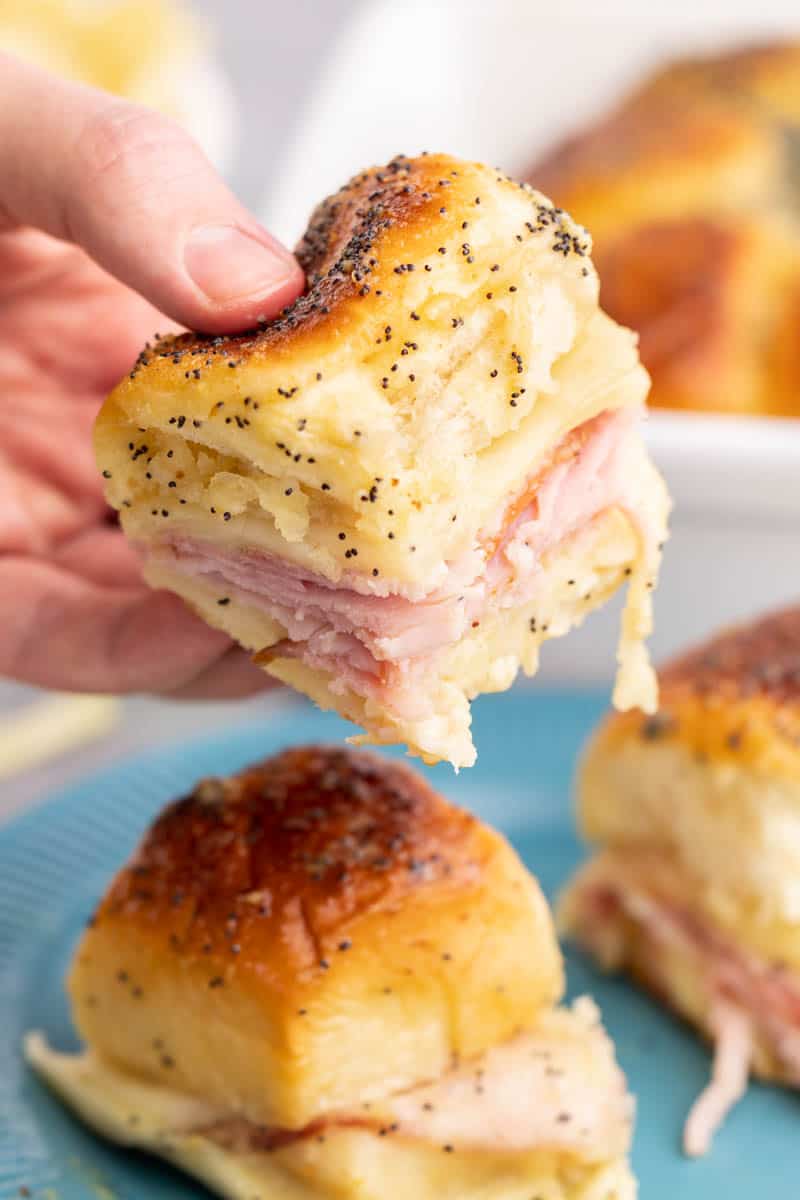 A hand holding up a ham and cheese slider.