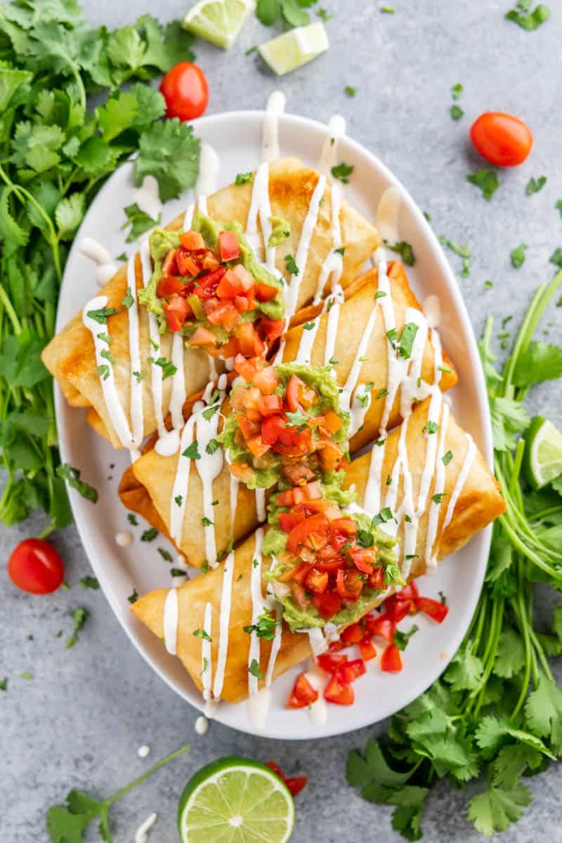 Overhead view of chimichangas on a serving platter with fresh cilantro and lime juice.