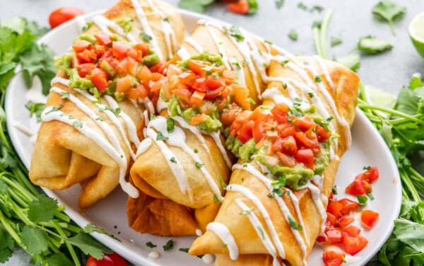 Overhead view of three chimichangas on a white serving platter.