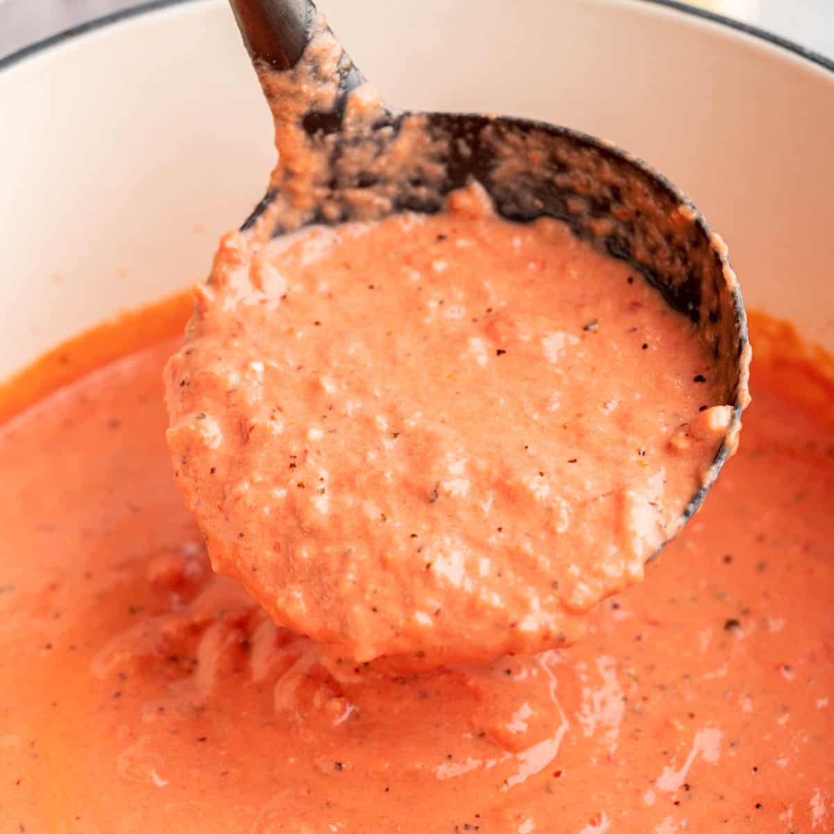 A close up view of a ladle of vodka sauce being scooped out of the pan.