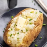 An air-fried baked potato served with butter and chives on a dinner plate.
