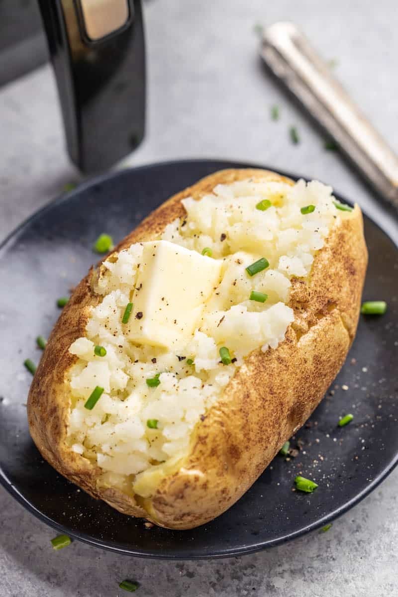 Air fried baked potato with butter and chives on a dinner plate.