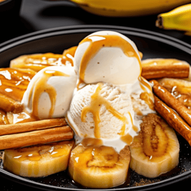 bananas foster on a black plate with vanilla ice cream on top and cinnamon sticks to garnish.
