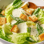 A bowl of caesar salad with homemade croutons, shaved parmesan, and black pepper.