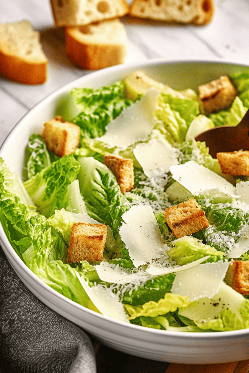 Caesar Salad in a large white bowl with shaved parmesan and homemade croutons.