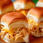 Cream Cheese Chicken sliders with melted cheddar cheese on a wooden cutting board.