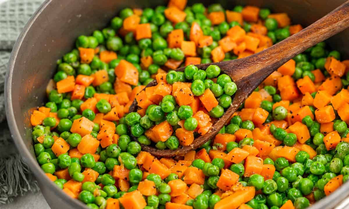 Peas and carrots in a pot with a wooden spoon.