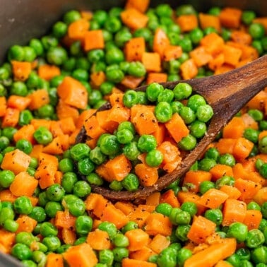 Peas and carrots in a pot with a wooden spoon.