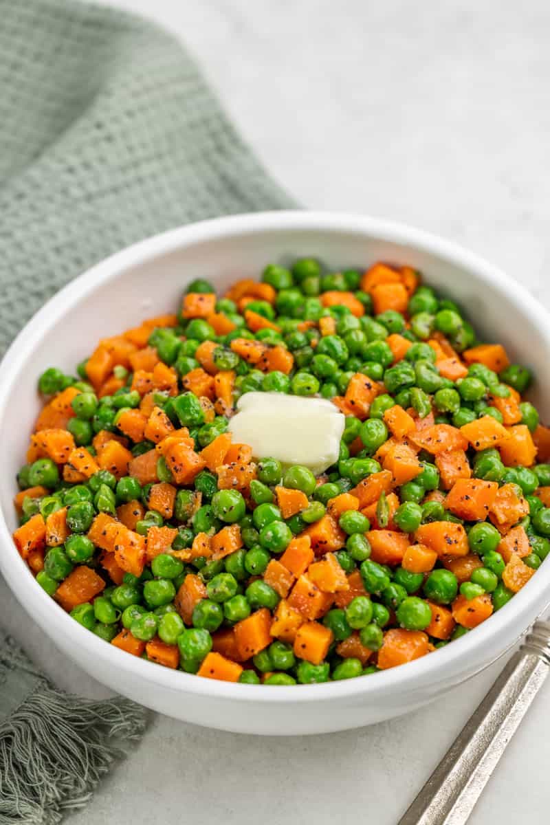A white bowl filled with peas and carrots with a pat of butter on top.
