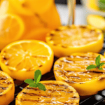 Grilled lemon halves with a pitcher of grilled lemonade in the background.