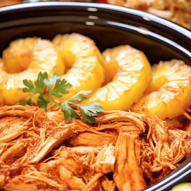 Shredded Hawaiian-style BBQ Chicken with sliced pineapple rings on top in a slow cooker.