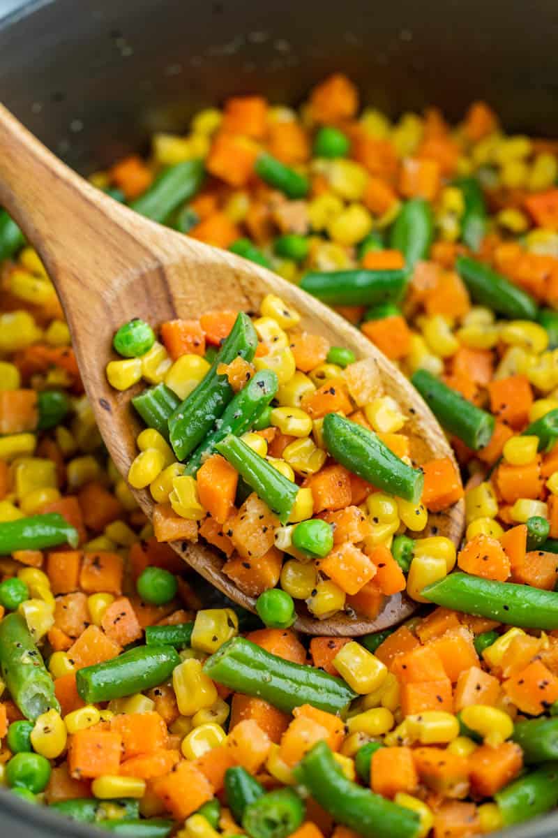 Close up view of mixed veggies in a wooden spoon.