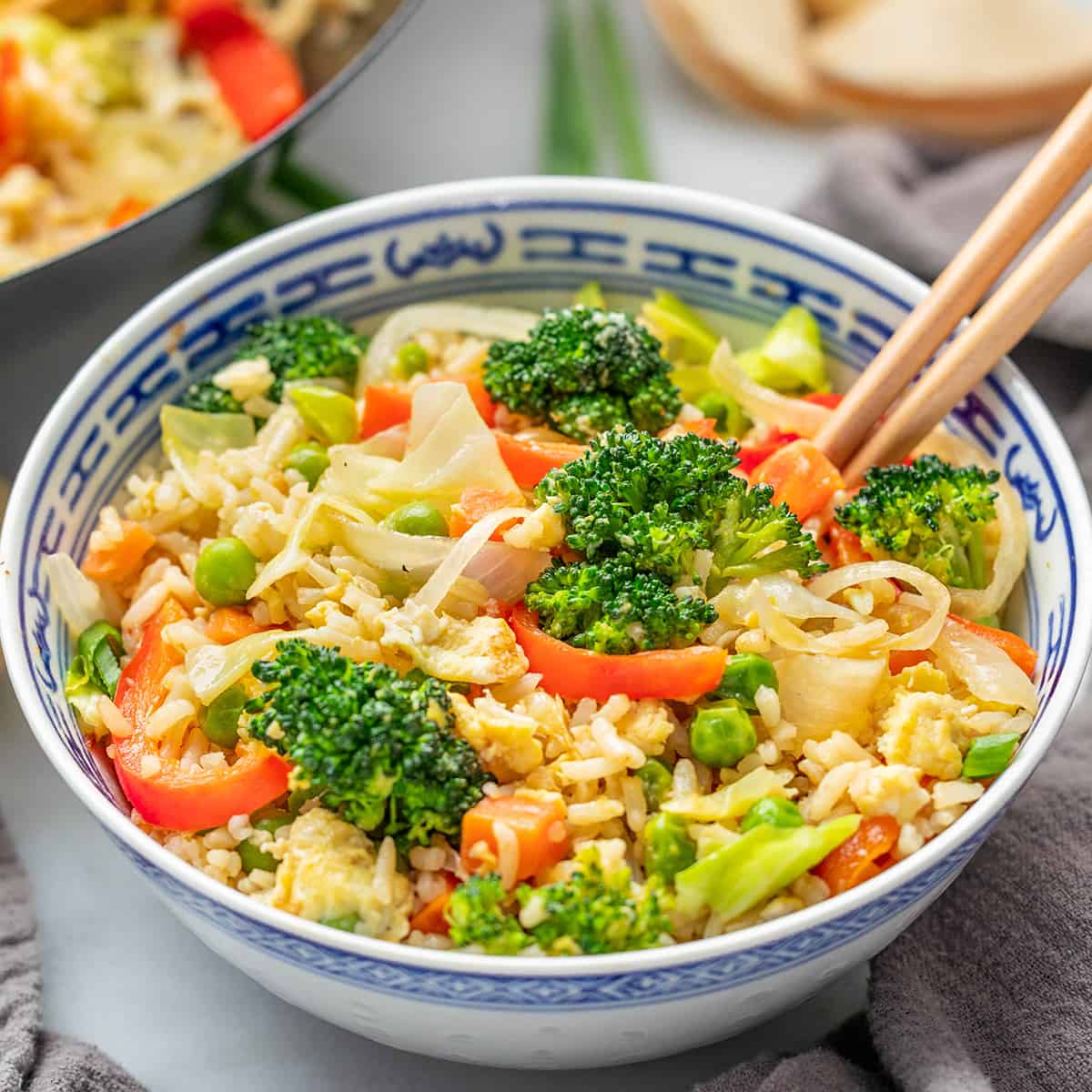 An overhead view of a bowl filled with take out vegetable fried rice with chop sticks.