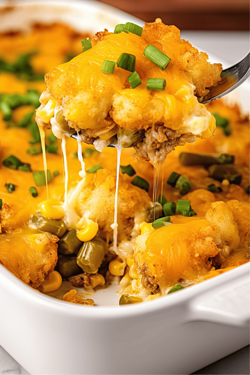A scoop of tater tot casserole being lifted from a casserole dish.