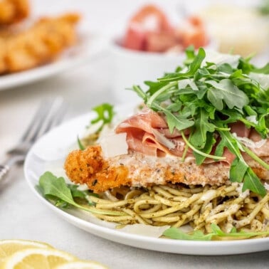 A plate with spaghetti, better than Bellagio chicken, and arugula on top.