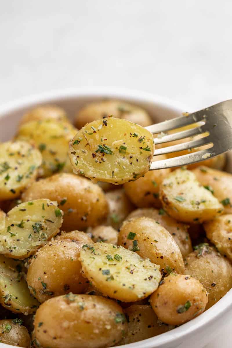 A fork stabbing into a boiled potato, being held above a bowl filled with them.